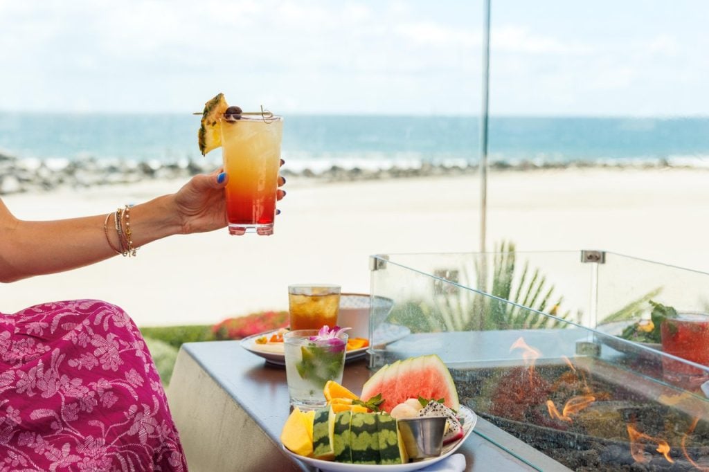 woman holding a tropical cocktail with food on a table
